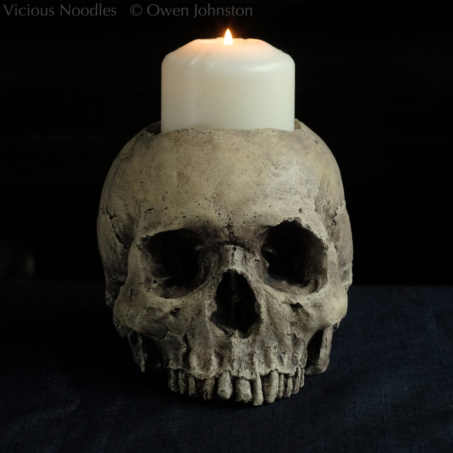 Human skull candle holder, without lower jaw, life size. It has a shallow hole on the top for a wide candle and is painted for a natural weathered look.