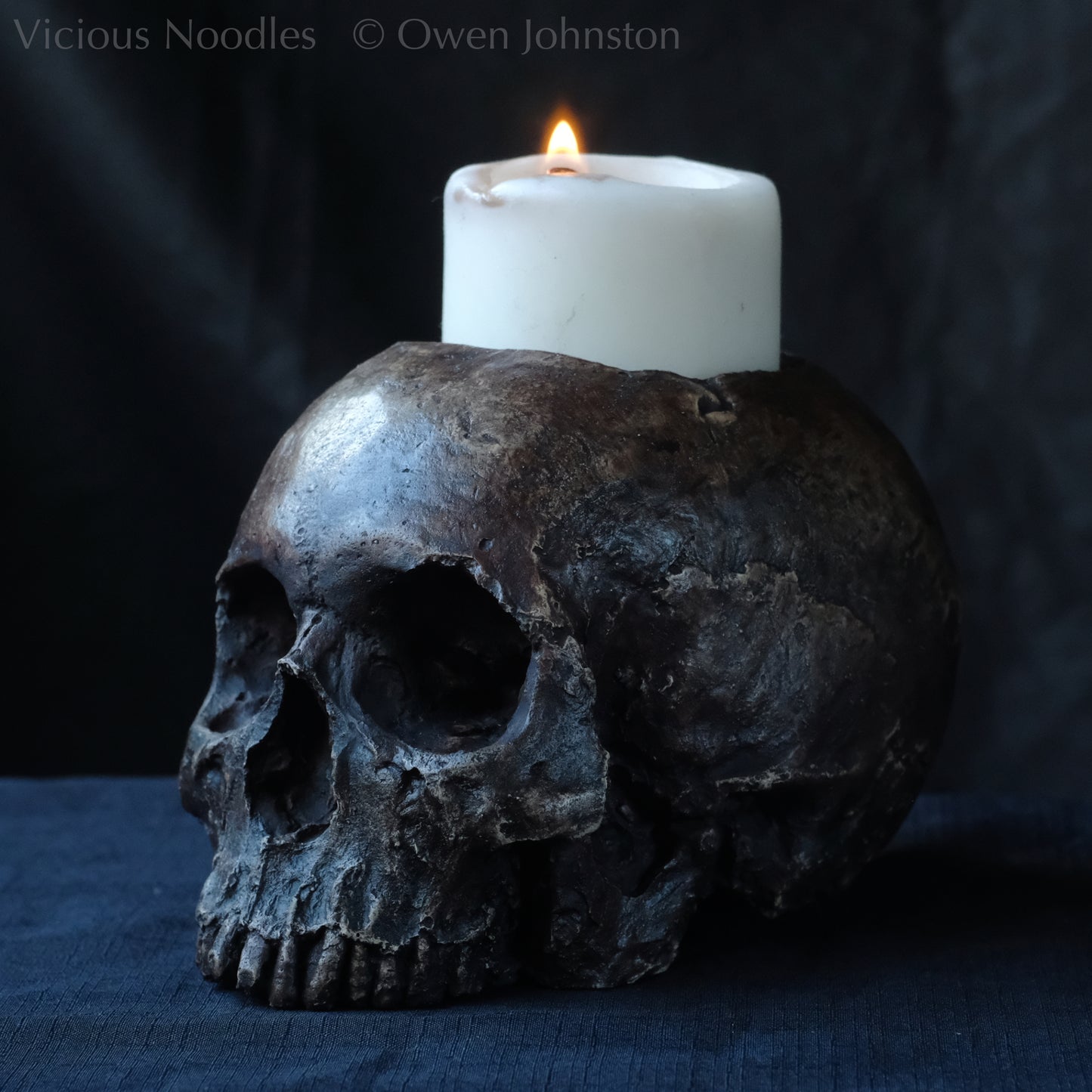 Human skull candle holder, without lower jaw, life size. It has a shallow hole on the top for a wide candle and is painted for a highly aged fossilised appearance with dark brown over lighter shades of brown. Lacquered for a polished finish.