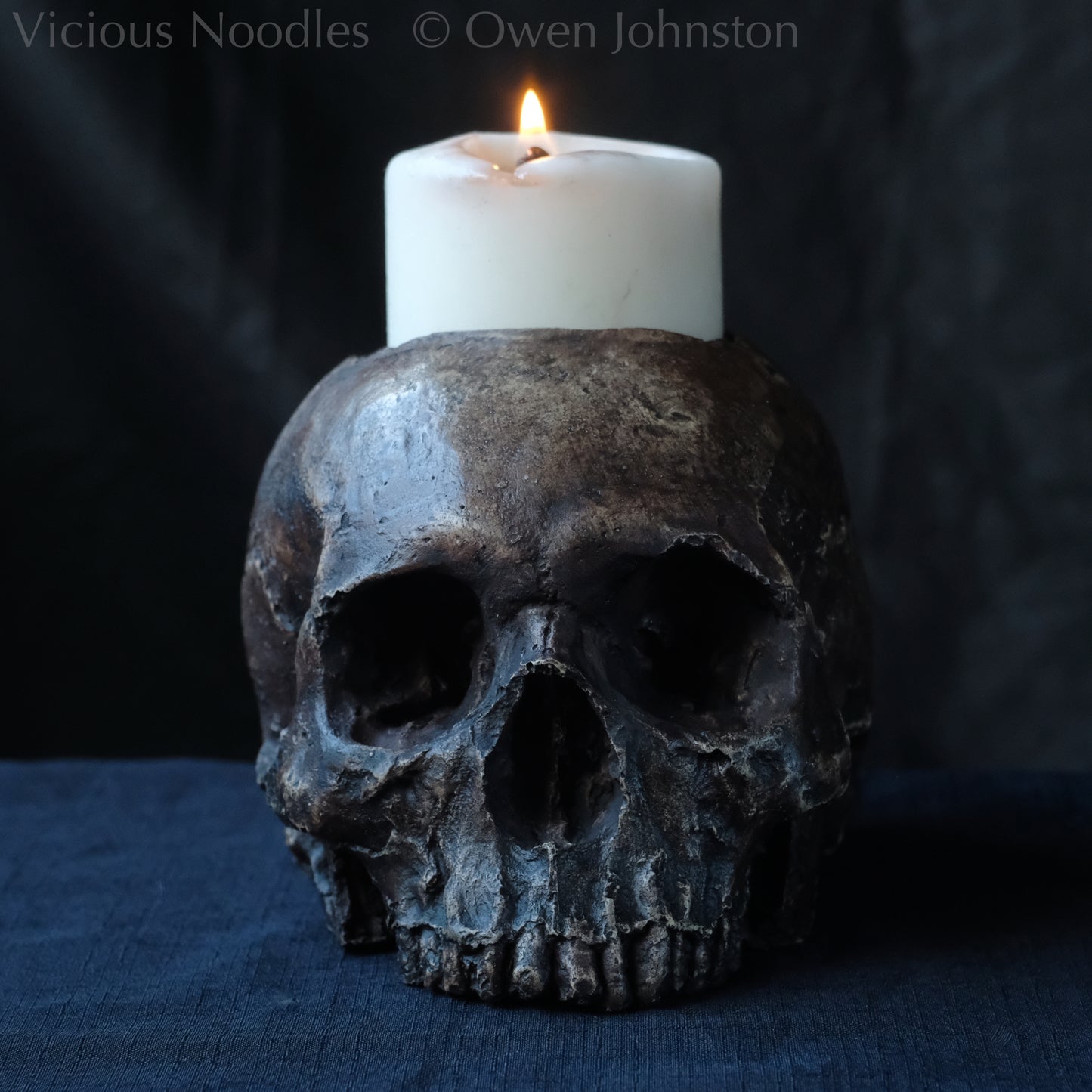 Human skull candle holder, without lower jaw, life size. It has a shallow hole on the top for a wide candle and is painted for a highly aged fossilised appearance with dark brown over lighter shades of brown. Lacquered for a polished finish.