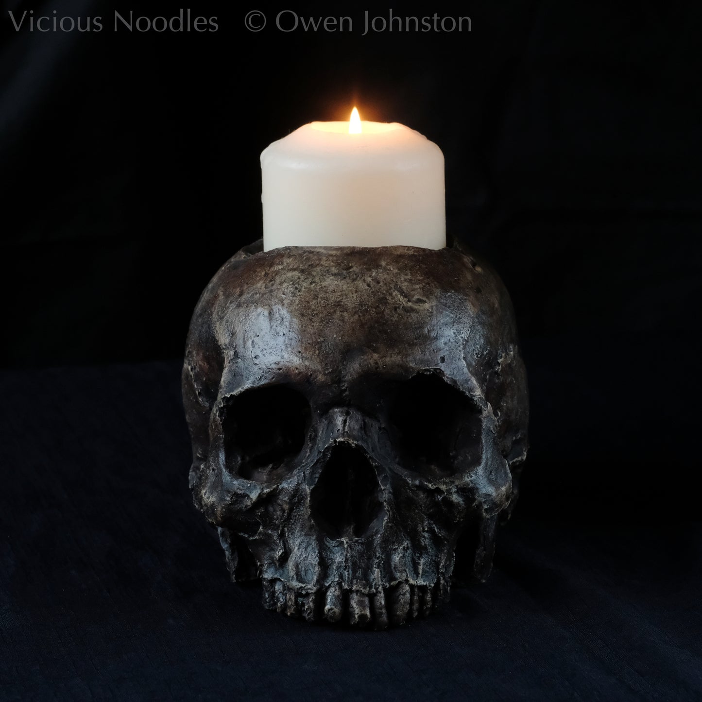 Human skull candle holder, without lower jaw, life size. It has a shallow hole on the top for a wide candle and is painted for a highly aged fossilised appearance with dark brown over lighter shades of brown. Lacquered for a polished finish.