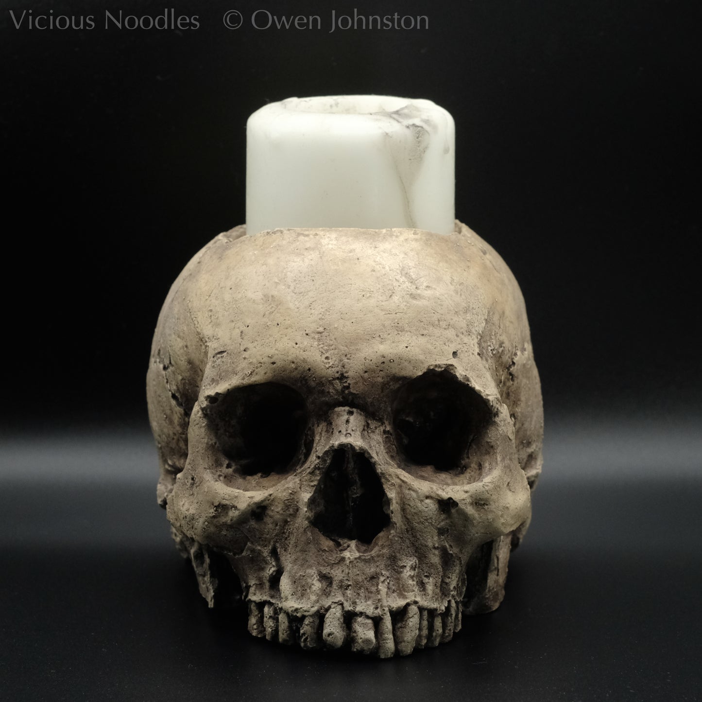 Human skull candle holder, without lower jaw, life size. It has a shallow hole on the top for a wide candle and is painted for a natural weathered look.