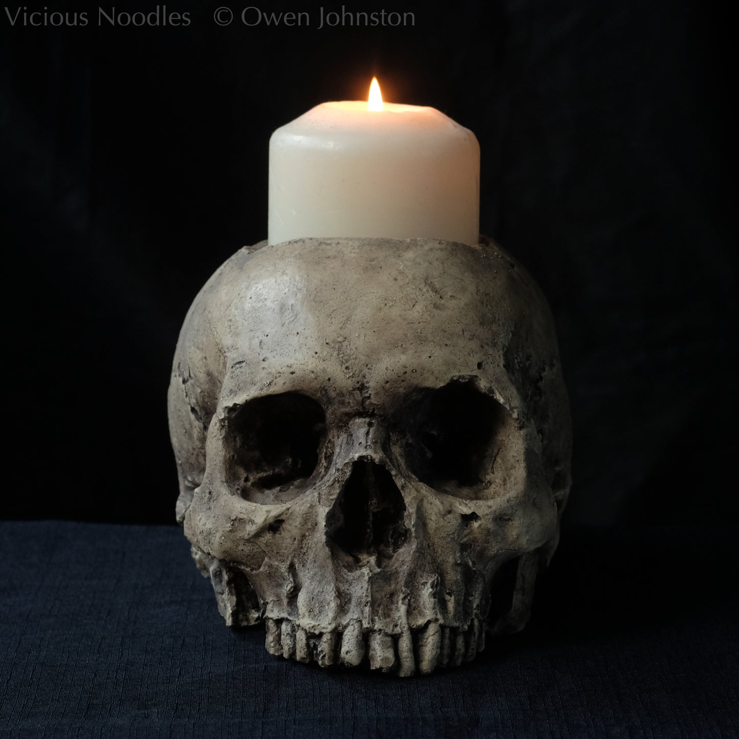 Human skull candle holder, without lower jaw, life size. It has a shallow hole on the top for a wide candle and is painted for a natural weathered look.